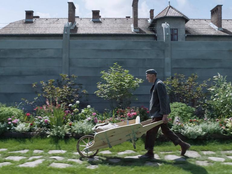 Ein Arbeiter schiebt eine Schubkarre vor dem Zaun, der das Anwesen des Auschwitz-Lagerkommandanten vom Vernichtungslager Auschwitz trennt.