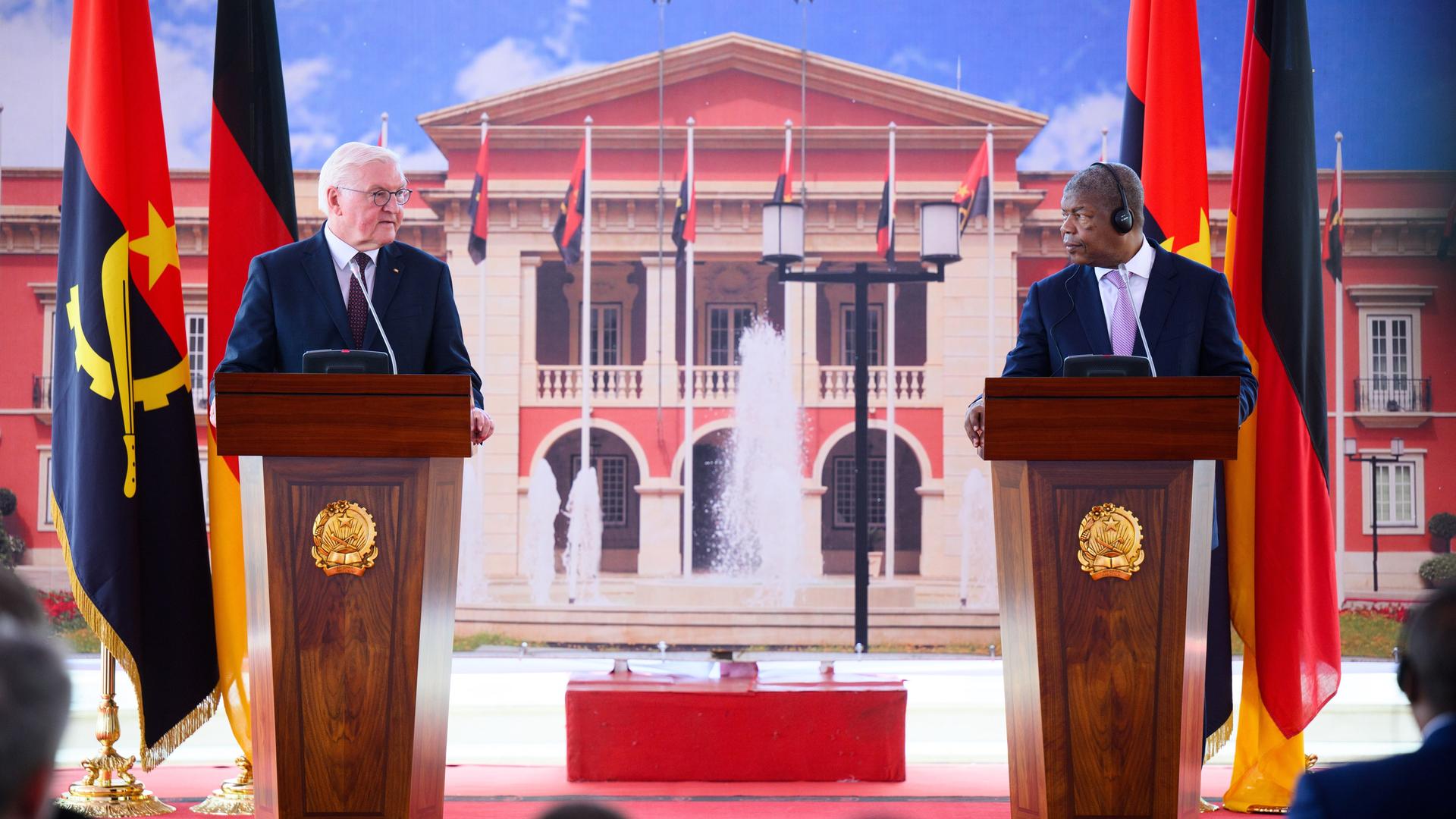 Die beiden stehen an den beiden Bildrändern vor dem rot-weißen Präsidentenpalast hinter Flaggen ihrer Länder an Rednerpulten.  
