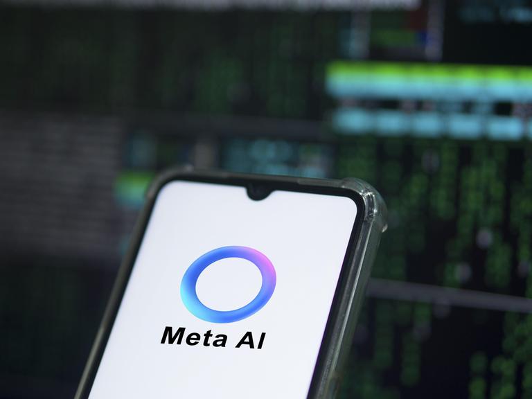 Auf einem Smartphone ist das Logo von Meta AI zu sehen: Ein überwiegend blauer Ring, der an manchen Stellen in Lila- und Grüntöne übergeht. 