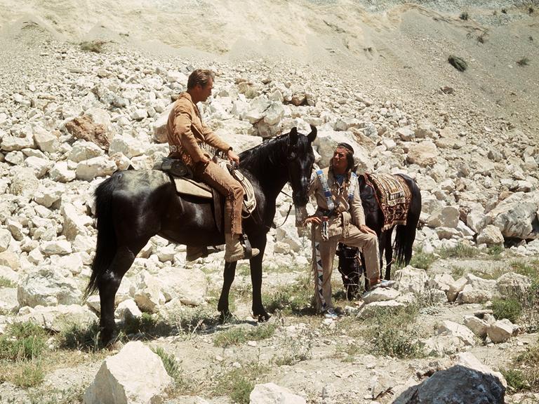 Der US-amerikanische Schauspieler Lex Barker als "Old Shatterhand" auf seinem Pferd zusammen mit Pierre Brice als "Winnetou" und dessen Pferd  in einer Szene der Karl-May-Verfilmung "Winnetou 3". 
