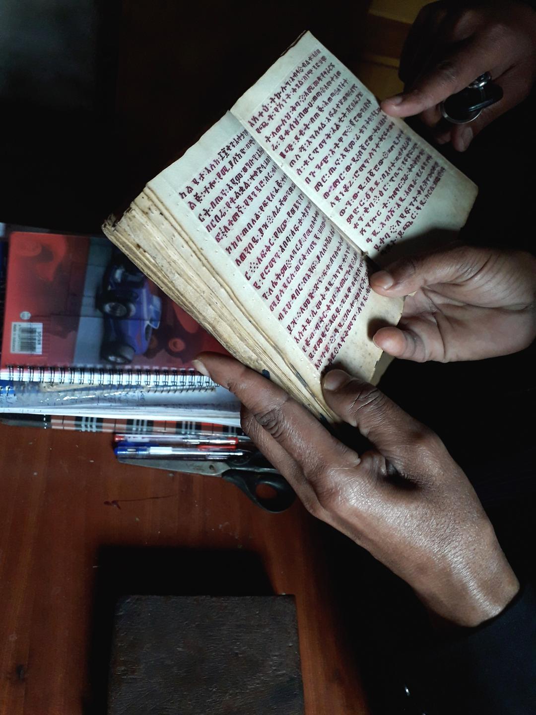 Heiler Tegistu hält ein kleines Buch aufgeklappt in seinen Händen.