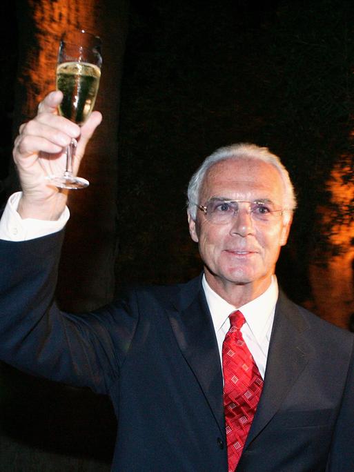 Archivbild: Franz Beckenbauer hält ein Glas Sekt in der Hand und prostet in die Luft.