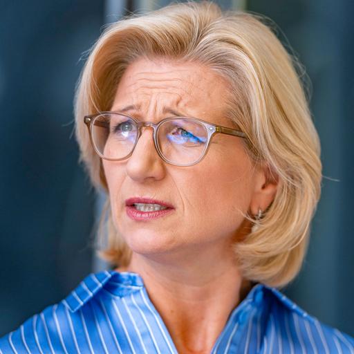 Porträt von Anke Rehlinger mit blonden Haaren und Brille. Sie trägt eine blaue Bluse und schaut nachdenklich.