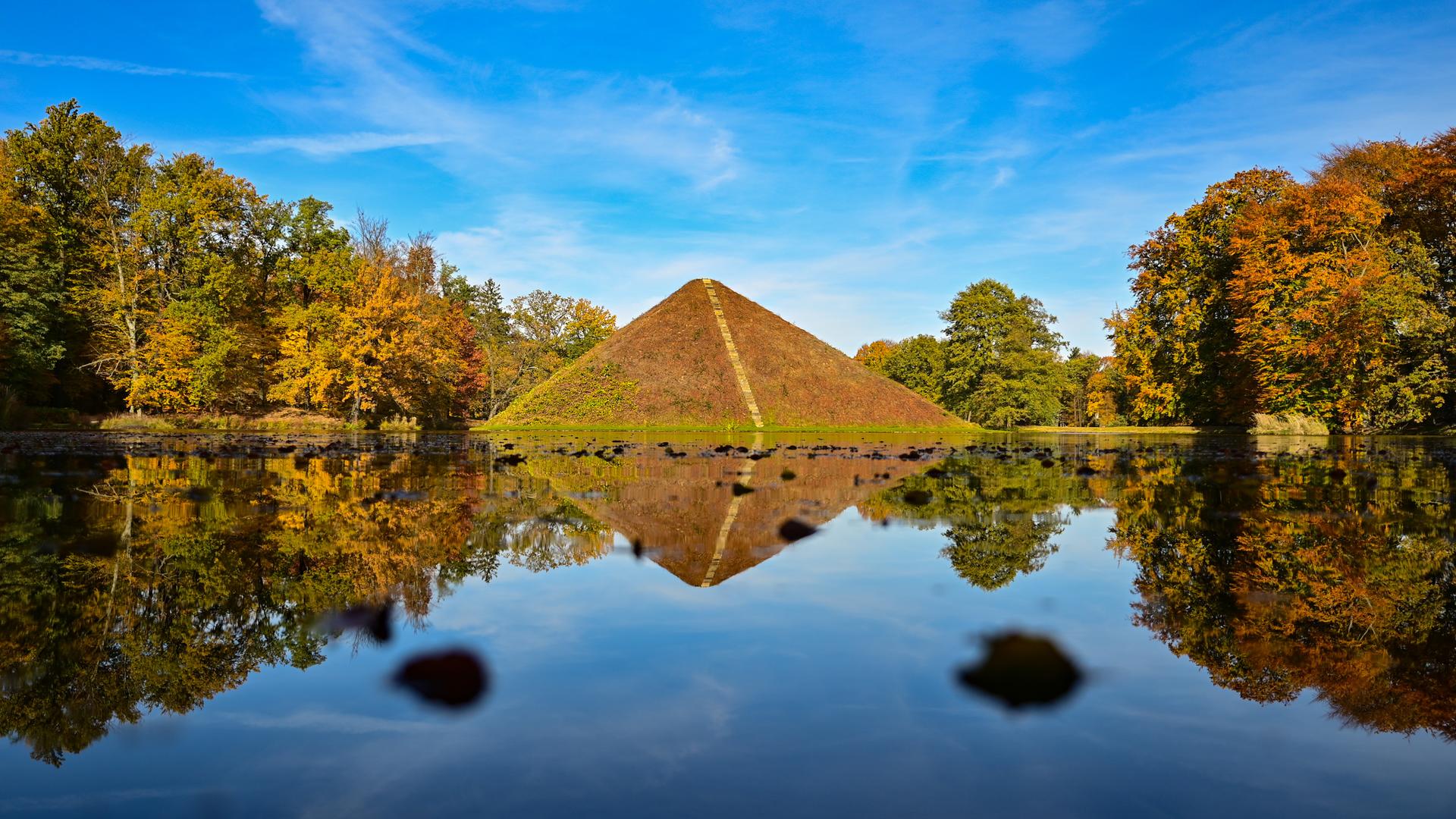 Eine bepflanzte Steinpyramide in einem See, der von herbstlich gefärbten Bäumen umstanden ist