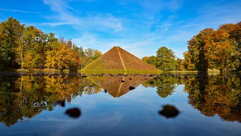 Eine bepflanzte Steinpyramide in einem See, der von herbstlich gefärbten Bäumen umstanden ist