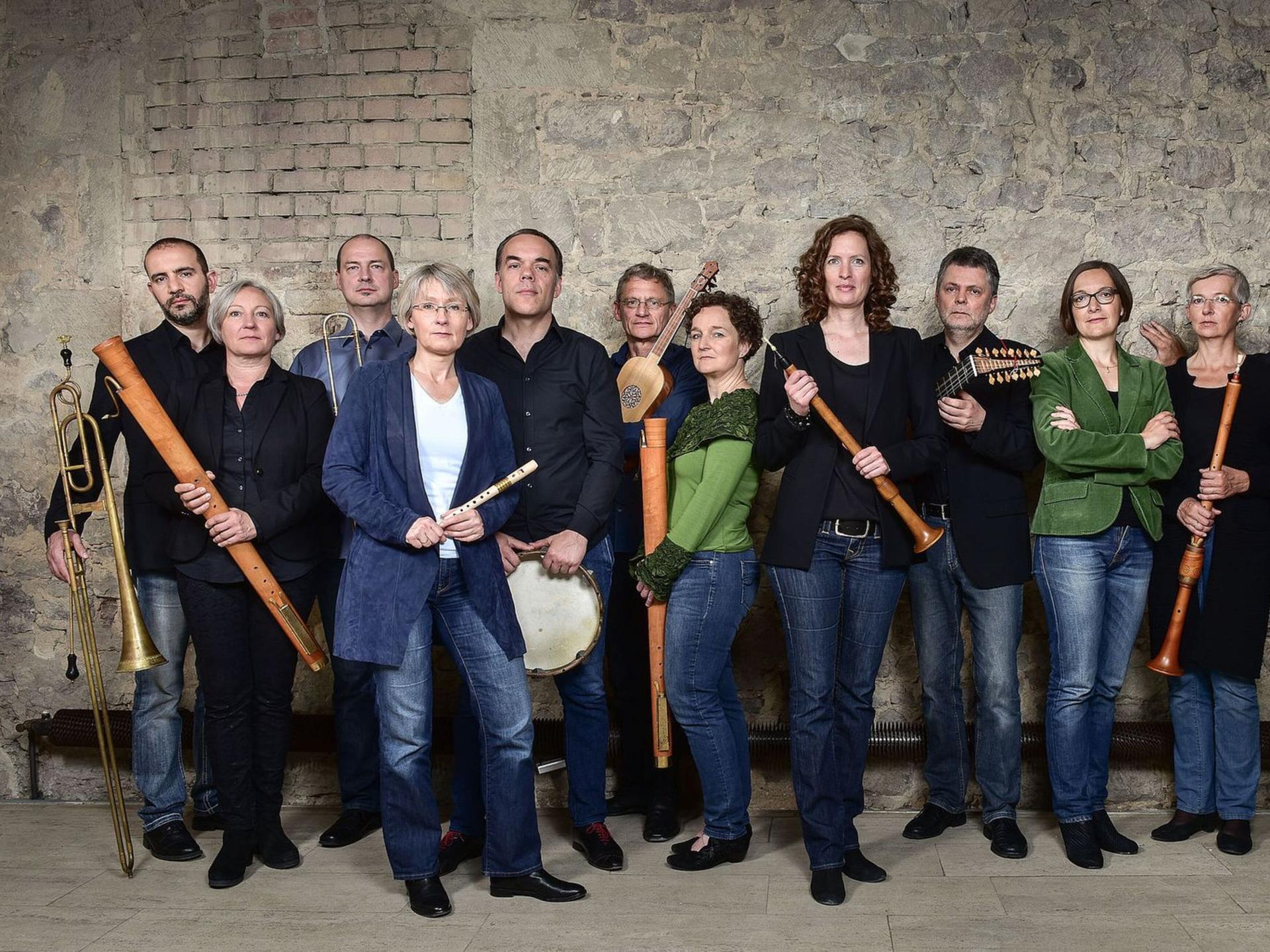 Mitglieder der Capella de la Torre stehen an einer historischen Ziegelwand mit ihren Instrumenten.