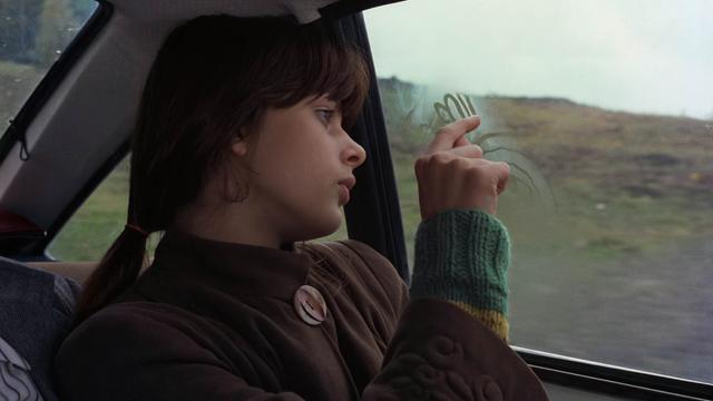 Ein Mädchen sitzt auf dem Rücksitz eines Autos und malt mit dem Finger an der beschlagenen Scheibe