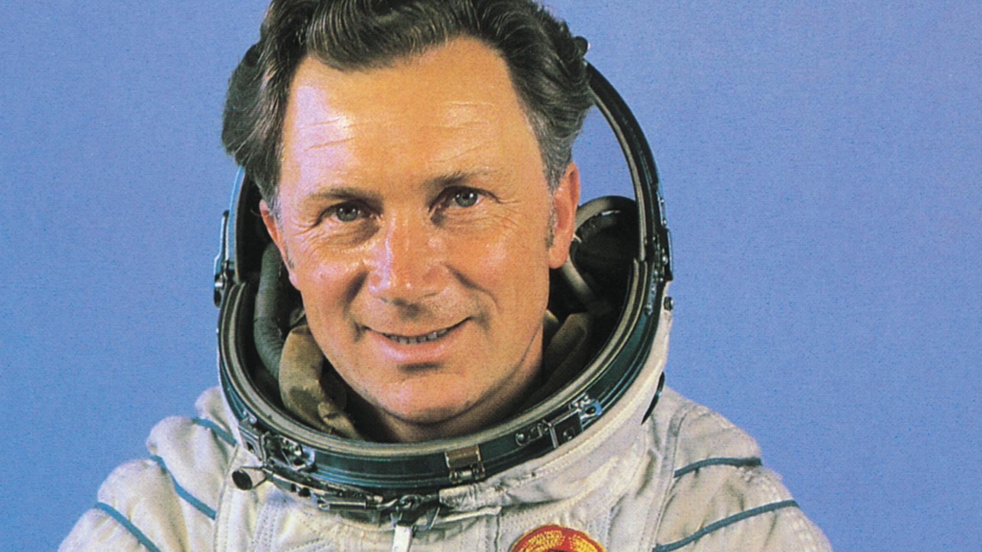Sigmund Jähn trägt seinen Kosmonautenanzug mit geöffnetem Visier und lächelt in die Kamera.