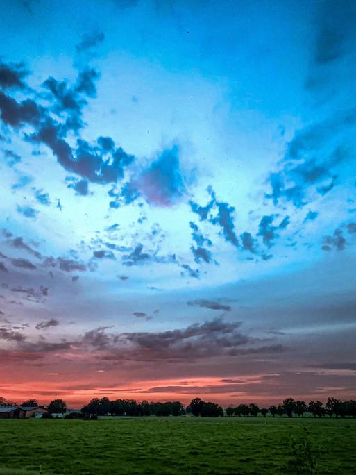 Ein dramatischer Sonnenuntergang über den wogenden Feldern mit wunderschön lebendigem und farbenfrohem Himmel.