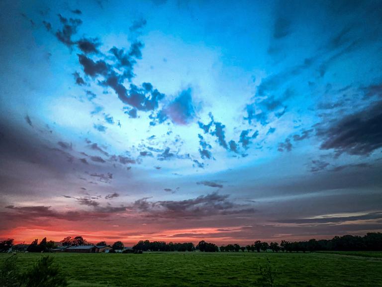 Ein dramatischer Sonnenuntergang über den wogenden Feldern mit wunderschön lebendigem und farbenfrohem Himmel.
