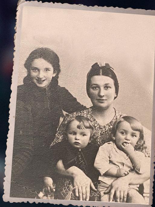 Das Bild zeigt eine alte, schwarzweiße Familienfotografie aus den frühen 1940er . Sie zeigt die dreijährigen Zwillinge Ida und Adam Paluch im Arm ihrer Mutter. Links im Bild ist ihre ältere Schwester Genia zu sehen. 