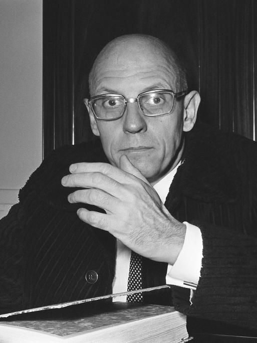 Foto (schwarz-weiß) des französischen Philosphen Michael Foucault, der an einem Schreibtisch sitzt, in die Kamera schaut und gestikuliert, Foto (schwarz-weiß) des französischen Philosphen Michael Foucault, der an einem Schreibtisch sitzt, in die Kamera schaut und gestikuliert,