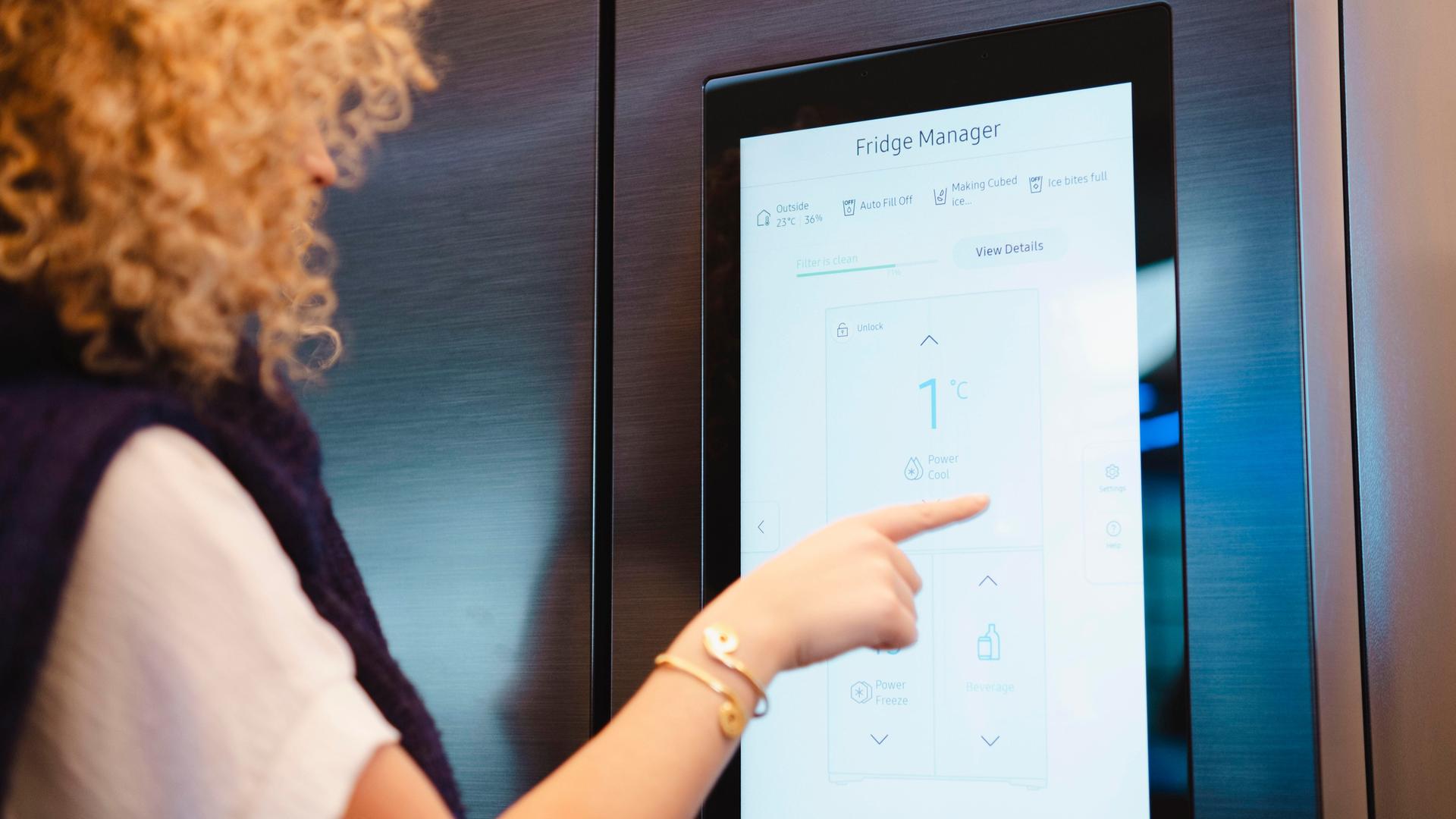 Eine Frau steht vor einem Kühlschrank mit modernem Touch Screen. Auf dem Bildschirm sind die Worte "Fridge Manager" zu lesen. Eine Frau steht vor einem Kühlschrank mit modernem Touch Screen. Auf dem Bildschirm sind die Worte "Fridge Manager" zu lesen.