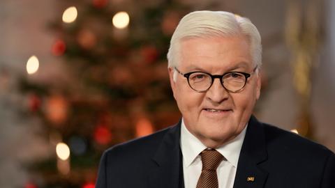Bundespräsident Frank-Walter Steinmeier steht vor einem Weihnachtsbaum und lächelt in die Kamera.