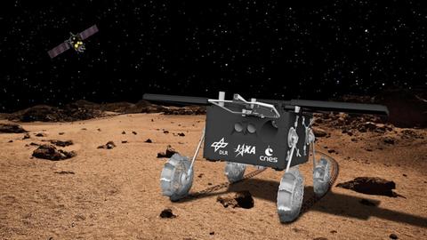 Eine Illustration zeigt einen Rover auf brauner Erde und im dunklen Himmel fliegt das MMX-Mutterschiff 