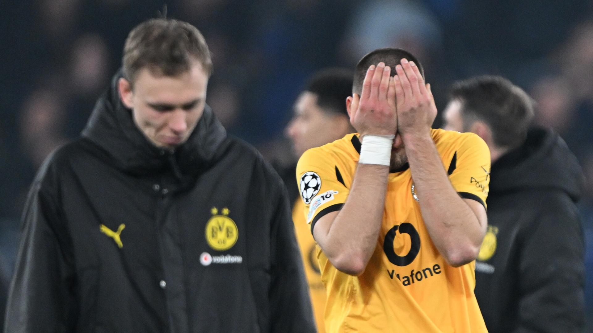 Anton im gelben Trikot hält beide Hände vors Gesicht. Dahinter unscharf ein weitere Dortmunder in einer dunklen Jacke mit hängendem Kopf. Anton im gelben Trikot hält beide Hände vors Gesicht. Dahinter unscharf ein weitere Dortmunder in einer dunklen Jacke mit hängendem Kopf.