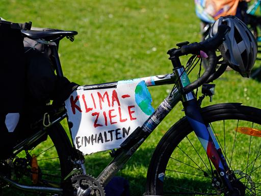 Ein Schild mit der Aufschrift "Klima-Ziele einhalten" hängt an einem Fahrrad.