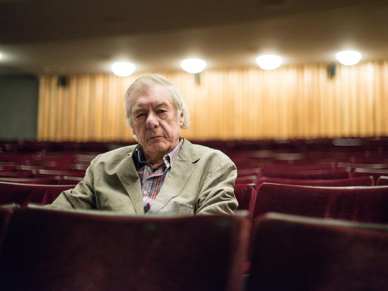 Regisseur Hans Neuenfels sitzt am 04.06.2015 nach einem Interview zu seiner Inszenierung von "Ariadne auf Naxos" in der Staatsoper im Schillertheater in einer roten Sitzreihe im Zuschauerraum.