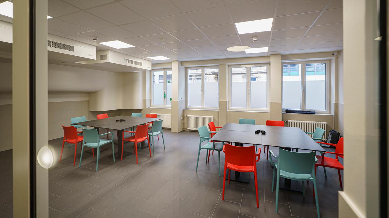 Blick in einen Raum mit großen Tischen mit mehreren Stühlen. An der Decke hängen Entlüftungsanlagen. Blick in einen Raum mit großen Tischen mit mehreren Stühlen. An der Decke hängen Entlüftungsanlagen.
