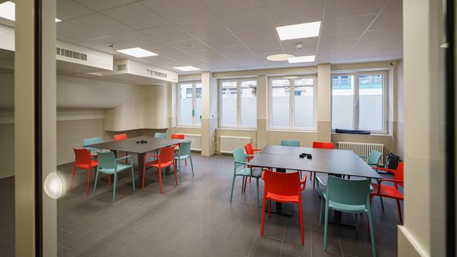 Blick in einen Raum mit großen Tischen mit mehreren Stühlen. An der Decke hängen Entlüftungsanlagen. Blick in einen Raum mit großen Tischen mit mehreren Stühlen. An der Decke hängen Entlüftungsanlagen.