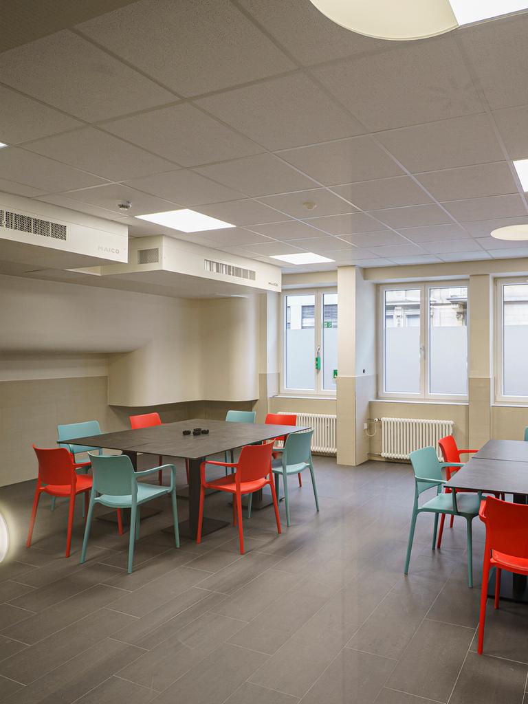 Blick in einen Raum mit großen Tischen mit mehreren Stühlen. An der Decke hängen Entlüftungsanlagen.