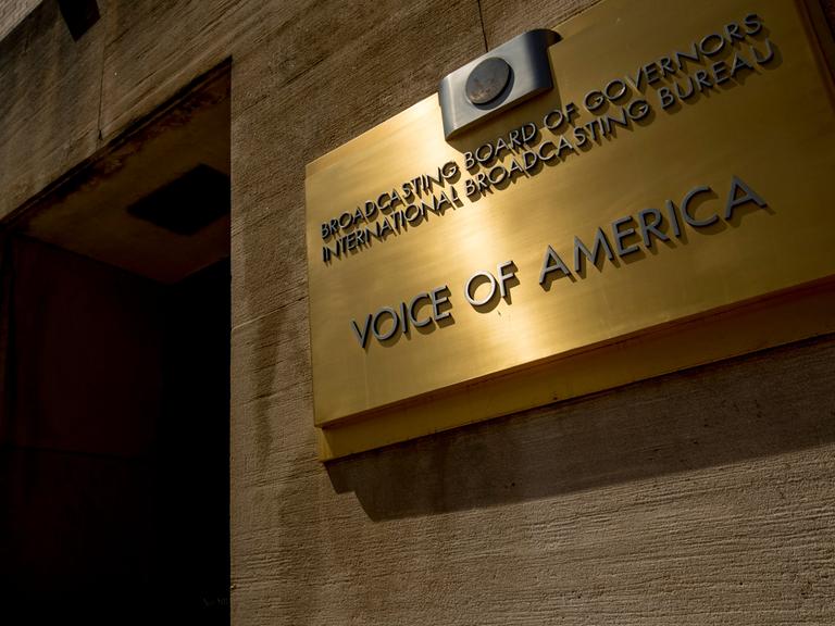 Das Bild zeigt ein goldfarbenes Schild mit der Aufschrift "Voice of America".