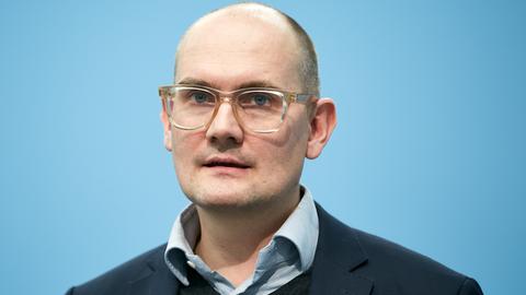 Janosch Dahmen ist vor einem blauen Hintergrund aufgenommen und schaut direkt in die Kamera.