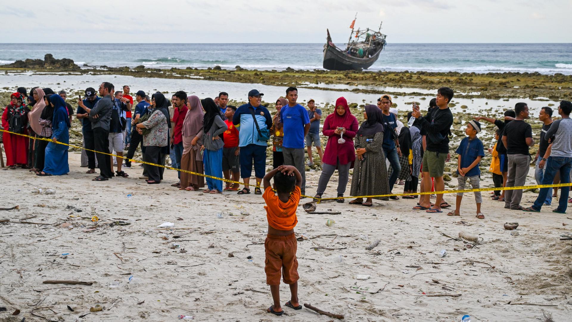 Rohingya-Flüchtlinge auf der Insel Sabang in der indonesischen Provinz Aceh. Sie stehen hinter einem Absperrband am Strand. Im Hintergrund ist ein Boot zu sehen.