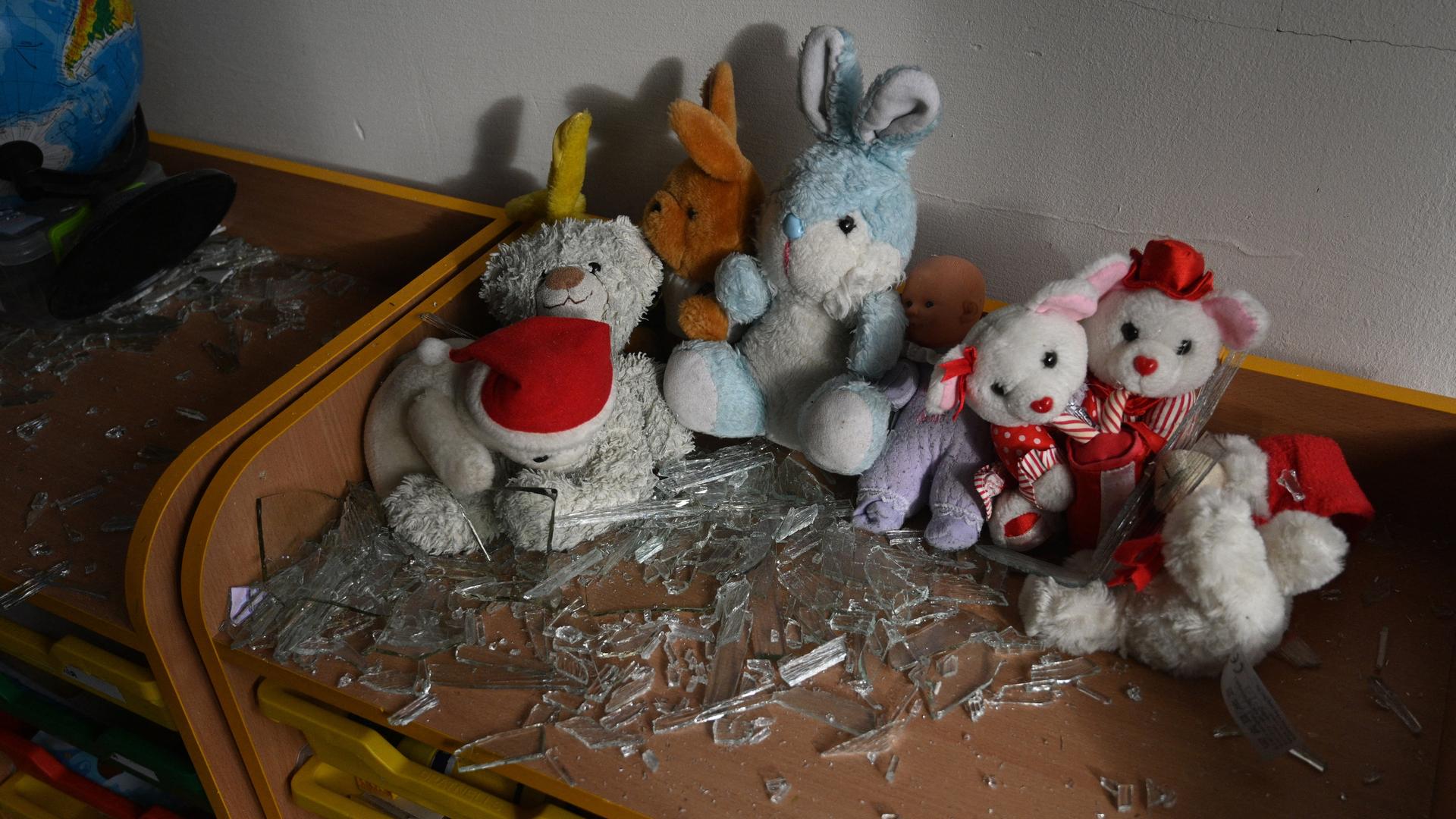 In einem Klassenraum liegen nach einem Bombenanschlag Kuscheltiere und Glassplitter auf einem Tisch.