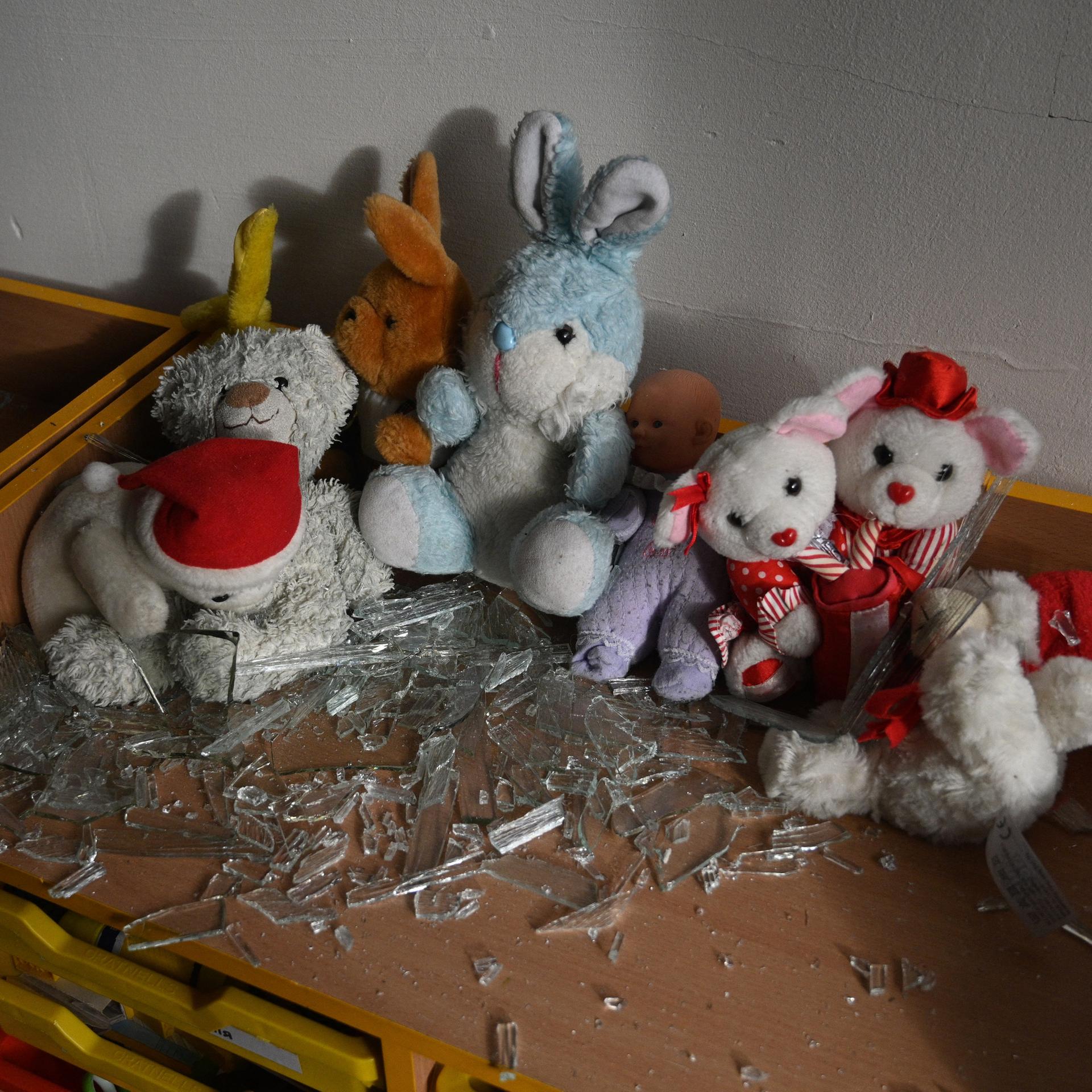 In einem Klassenraum liegen nach einem Bombenanschlag Kuscheltiere und Glassplitter auf einem Tisch.