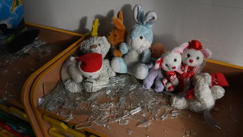 In einem Klassenraum liegen nach einem Bombenanschlag Kuscheltiere und Glassplitter auf einem Tisch.