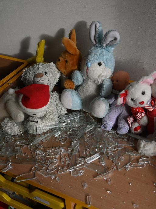 In einem Klassenraum liegen nach einem Bombenanschlag Kuscheltiere und Glassplitter auf einem Tisch.