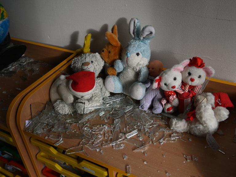 In einem Klassenraum liegen nach einem Bombenanschlag Kuscheltiere und Glassplitter auf einem Tisch.