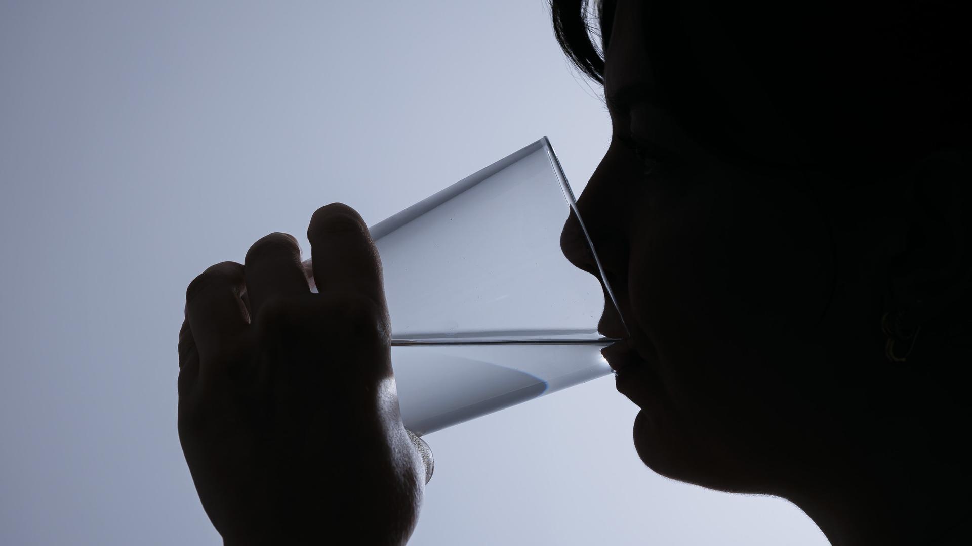 Symbolfoto: Silhouette einer Frau, die ein Glas Leitungswasser trinkt.