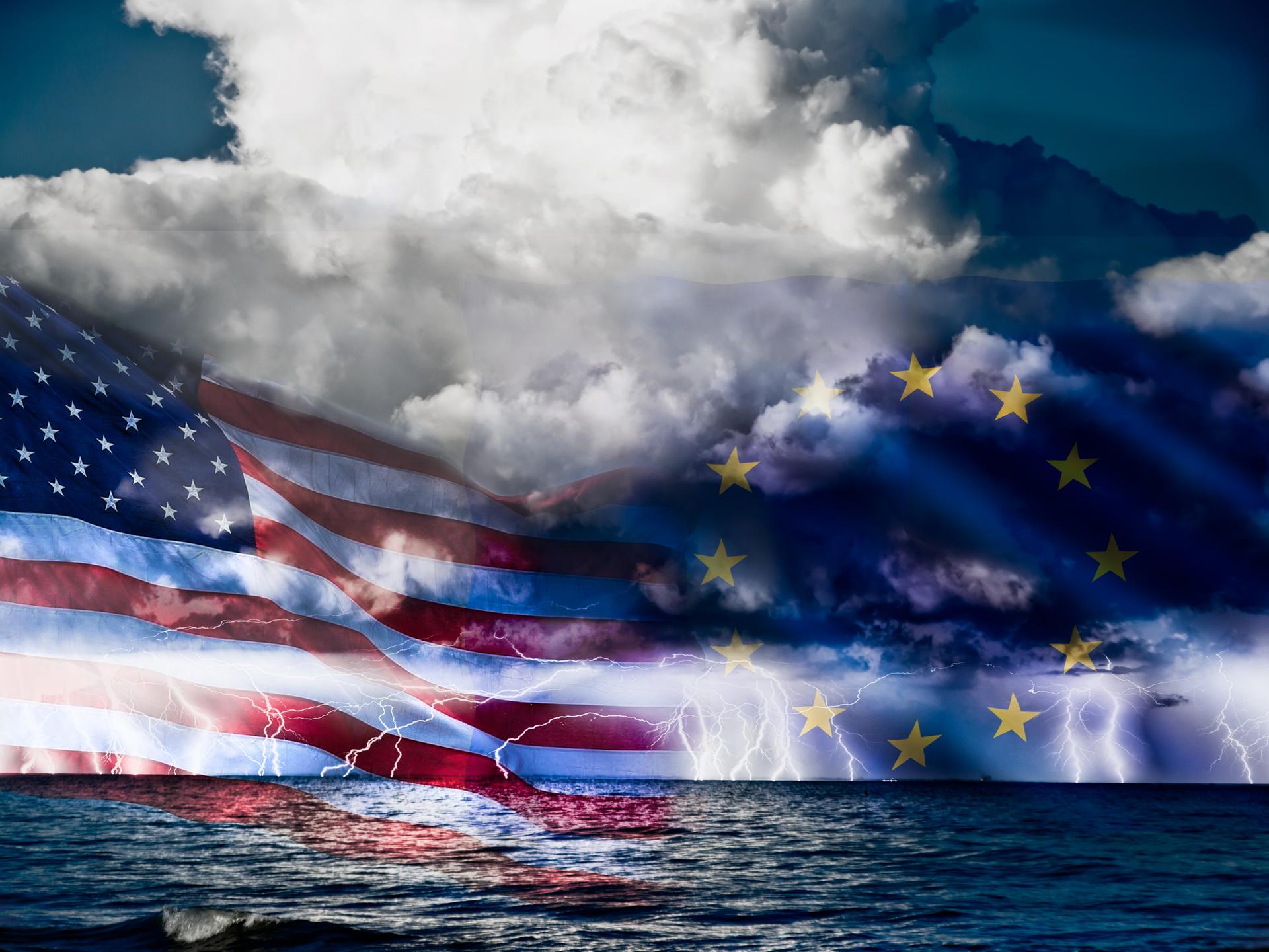 Die Flagge der USA und die Flagge der EU in einer Bildcollage auf stürmischer See. Im Hintergrund ziehen dunkle Wolken auf.