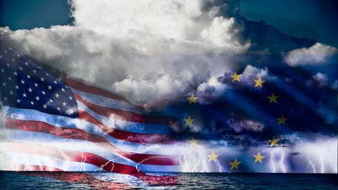 Die Flagge der USA und die Flagge der EU in einer Bildcollage auf stürmischer See. Im Hintergrund ziehen dunkle Wolken auf.