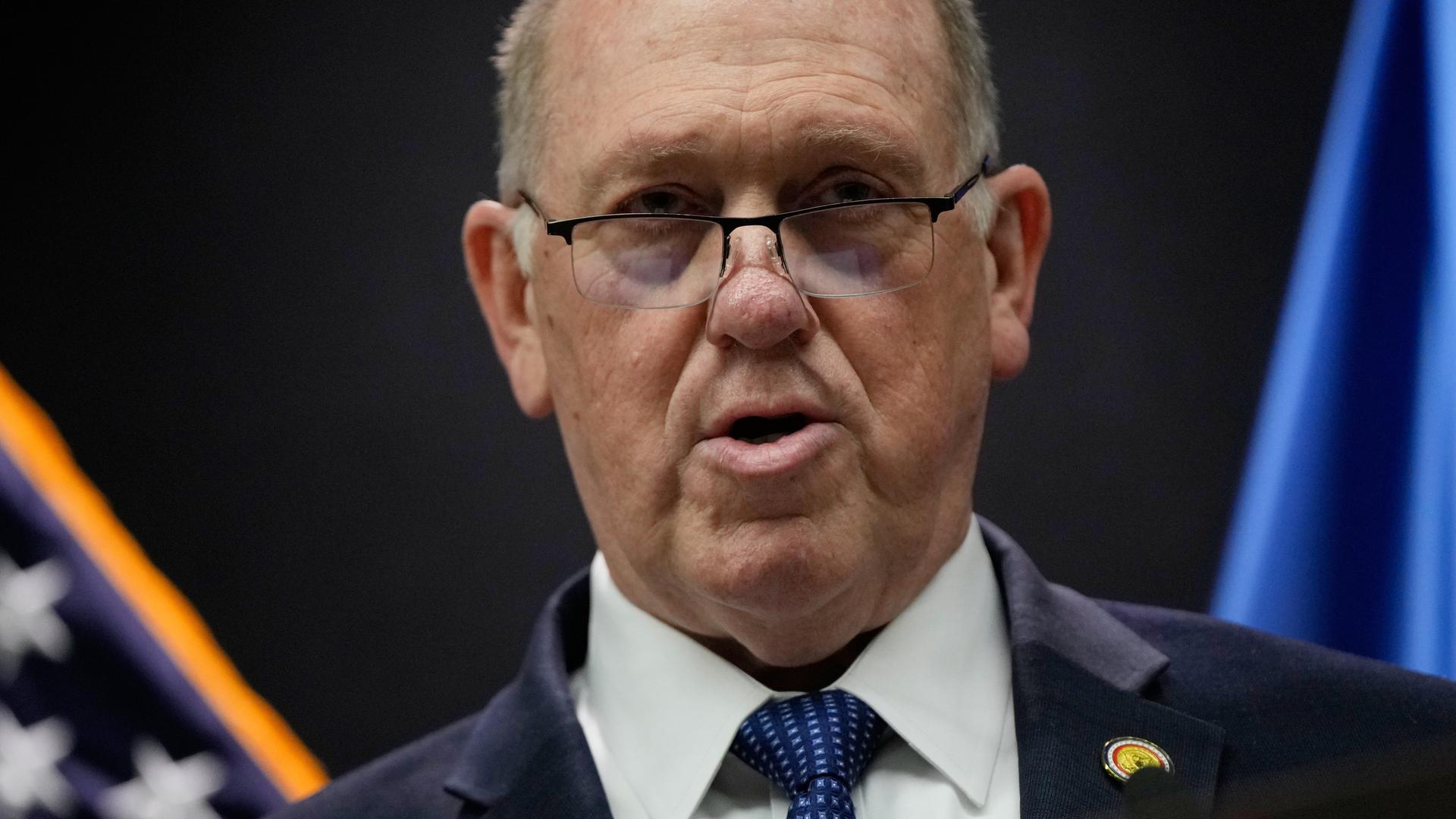 Tom Homan schaut bei einer Pressekonferenz in Minneapolis in die Kamera. Er trägt ein weißes Hemd, eine Anzugjacke und eine blaue Krawatte.