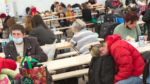 Erschöpfte ukrainische Flüchtlinge sitzen im Willkommenszelt am Berliner Hauptbahnhof auf Holzbänken. 