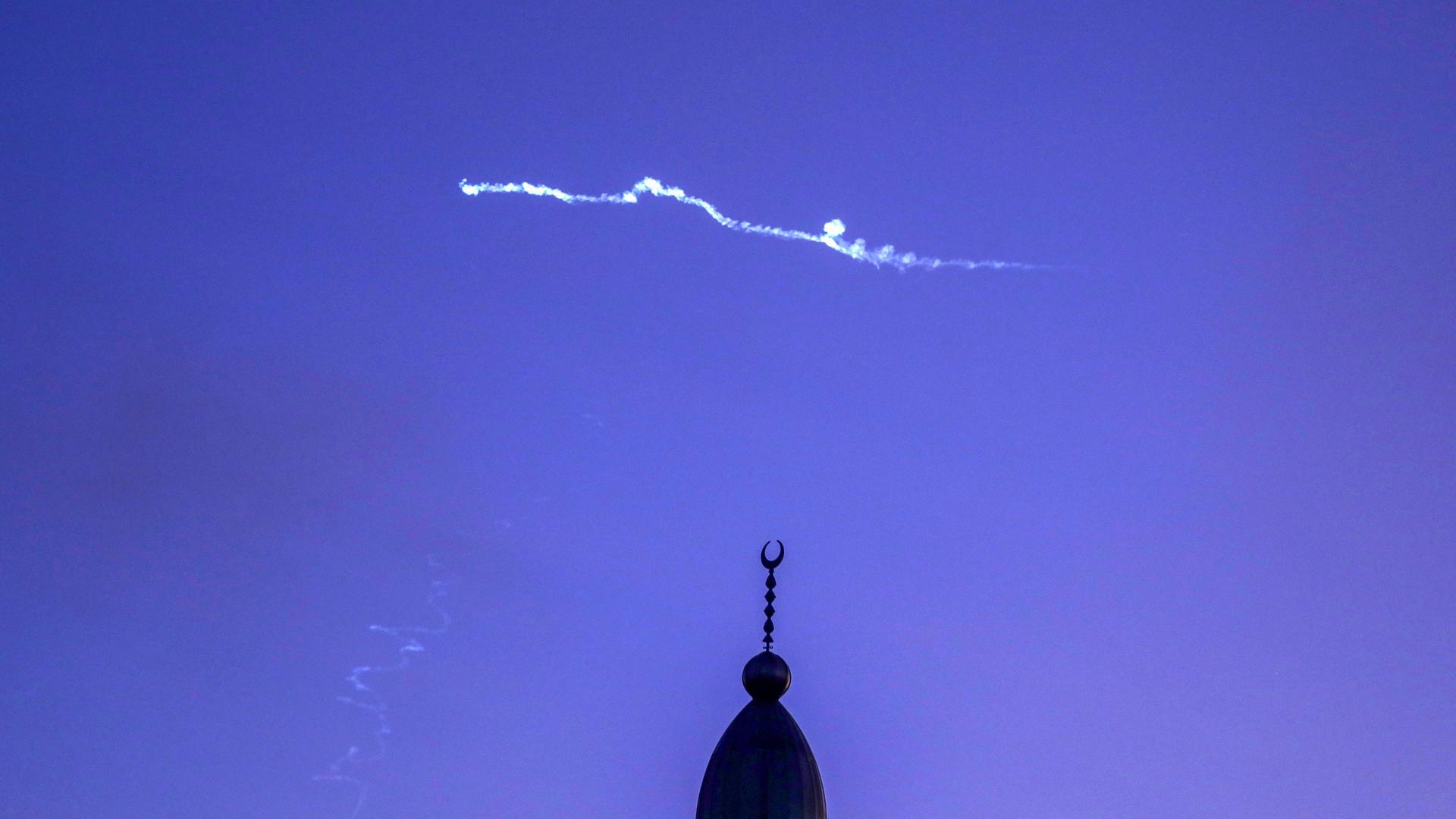 Am Himmel sind die Rauchschwaden einer Rakete zu erkennen, am Boden die Spitze einer Moschee. Am Himmel sind die Rauchschwaden einer Rakete zu erkennen, am Boden die Spitze einer Moschee.