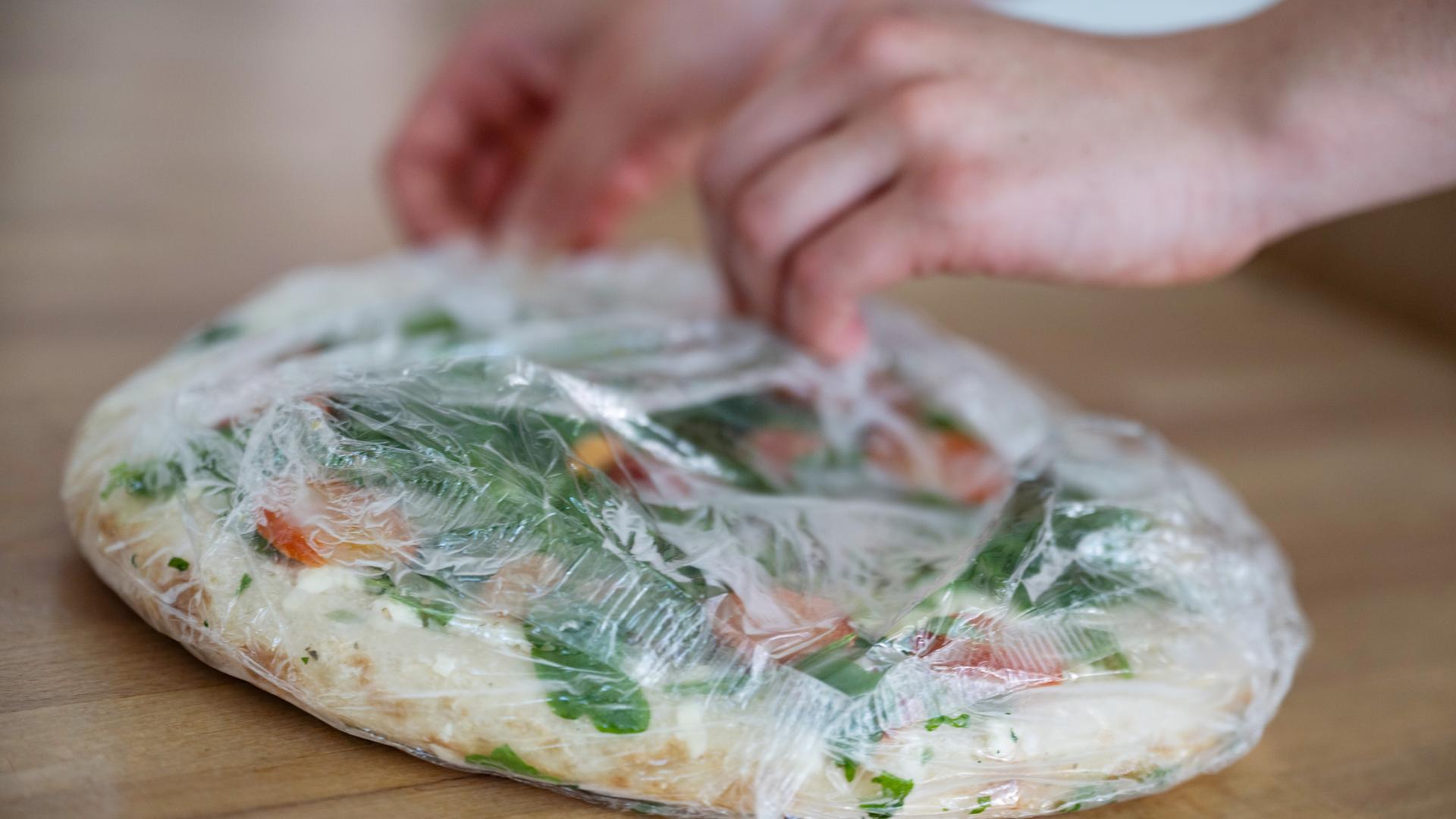 Hände packen eine tiefgekühlte Pizza aus.