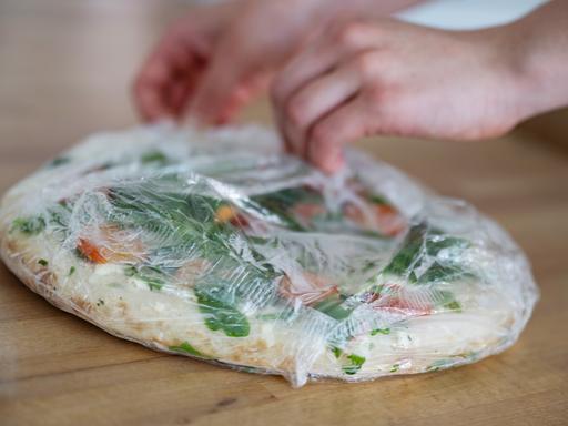 Hände packen eine tiefgekühlte Pizza aus.