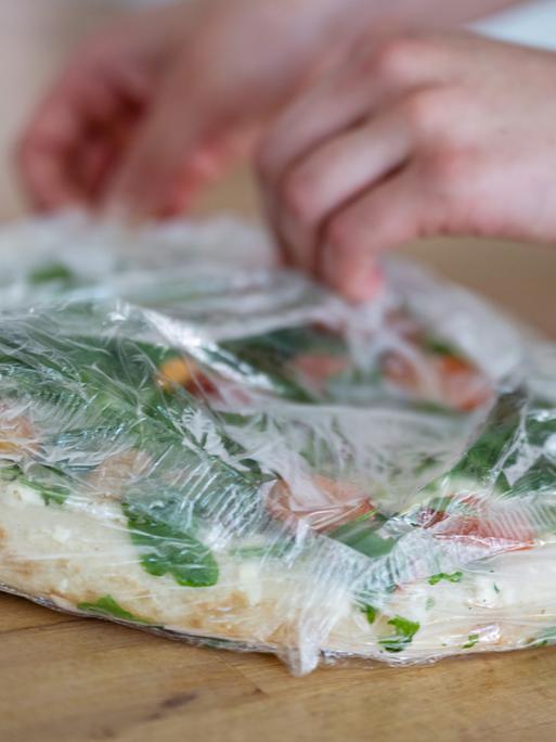 Hände packen eine tiefgekühlte Pizza aus.