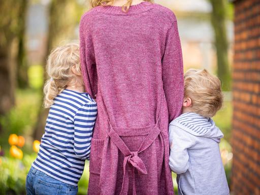 Zu sehen ist eine Frau von hinten, an die sich jeweils ein Junge und ein Mädchen anschmiegen. Vermutlich Sohn und Tochter. Zu sehen ist eine Frau von hinten, an die sich jeweils ein Junge und ein Mädchen anschmiegen. Vermutlich Sohn und Tochter.