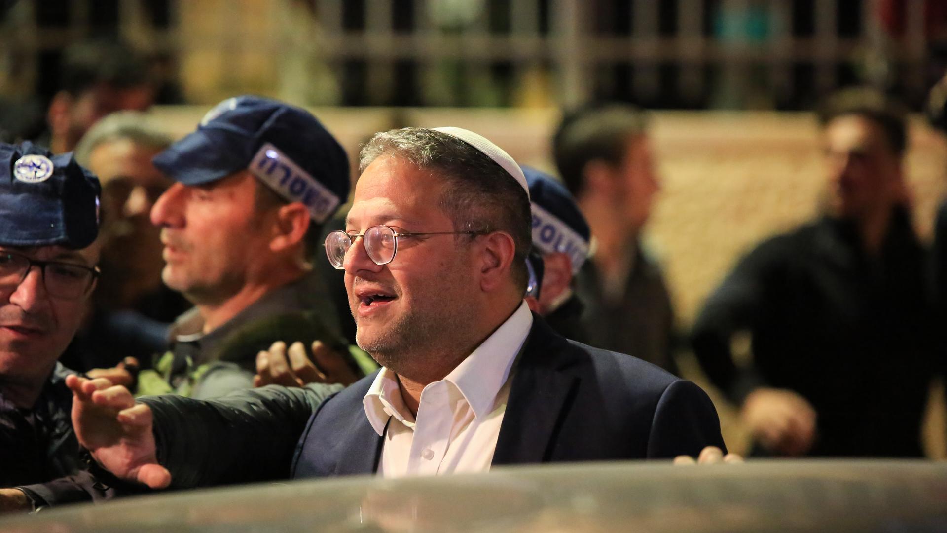 Israels Sicherheitsminister Itamar Ben-Gvir steht zwischen isralischen Polizisten nachts auf der Straße Israels Sicherheitsminister Itamar Ben-Gvir steht zwischen isralischen Polizisten nachts auf der Straße
