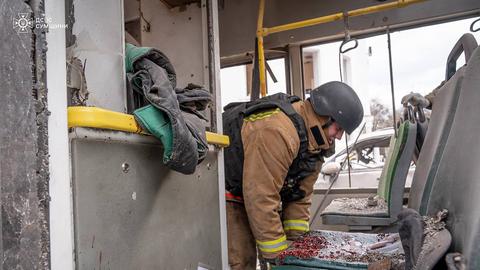 Ein ukrainischer Helfer arbeitet in einem Bus, der von russischen Angriffen zerstört wurde. Der Innenraum des Busses ist völlig demoliert. 