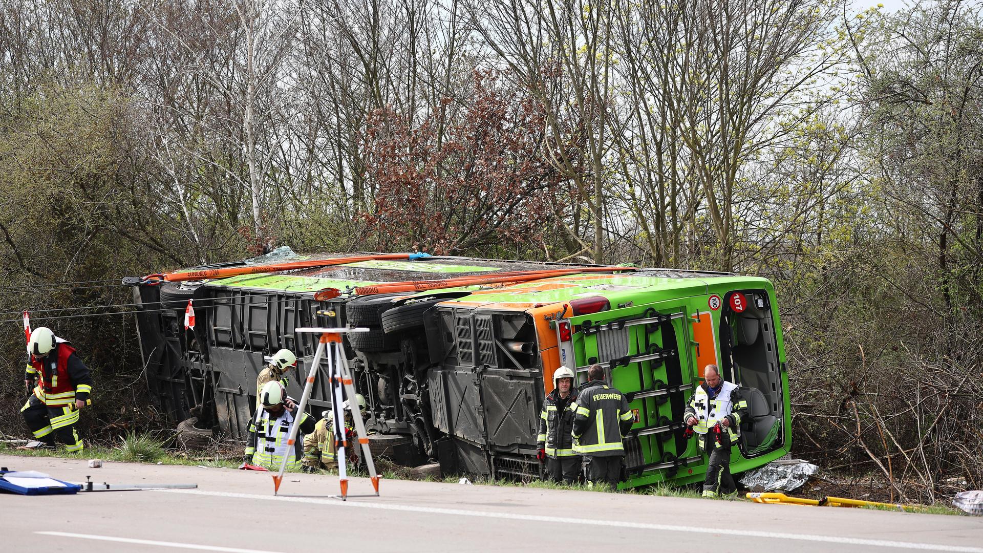 Ein Reisebus liegt zur Seite gekippt an der Unfallstelle auf der A9, daneben stehen Rettungskräfte.