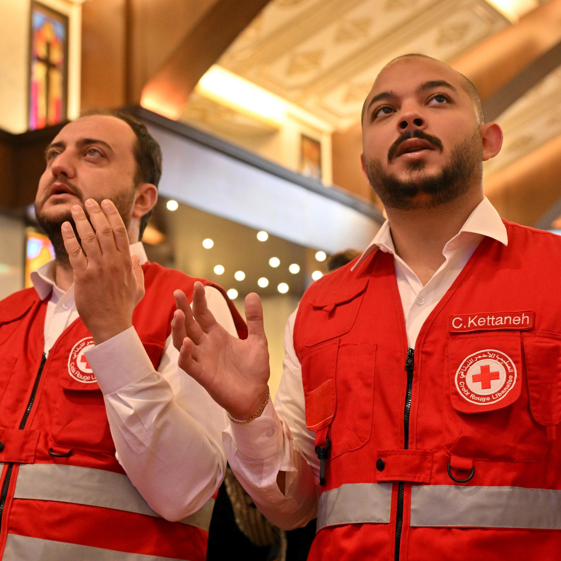 Libanesische Rettungskräfte beten in einer Kirche für fünf Menschen, die bei Angriffen im Norden Beiruts getötet wurden. Die beiden Männer blicken ernst und heben die Hände zum Gebet.