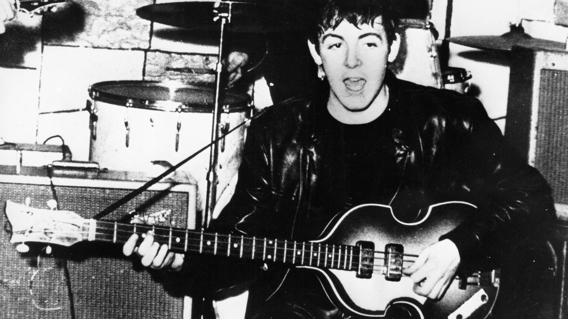 Schwarz-weiß-Aufnahme von Paul McCartney im Jahr 1961 in Hamburg. Er singt und spielt Gitarre.