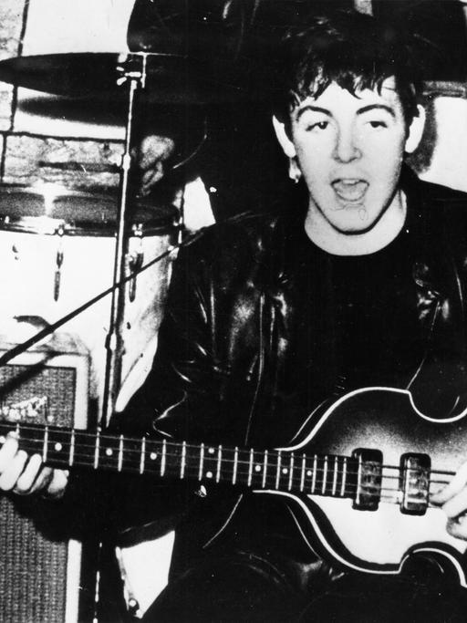 Das schwarz-weiß Foto zeigt den Beatles-Sänger Paul McCartney mit seiner Bass-Gitarre.