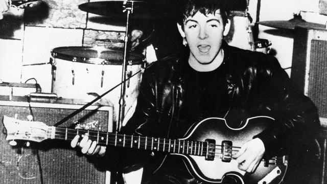 Das schwarz-weiß Foto zeigt den Beatles-Sänger Paul McCartney mit seiner Bass-Gitarre.